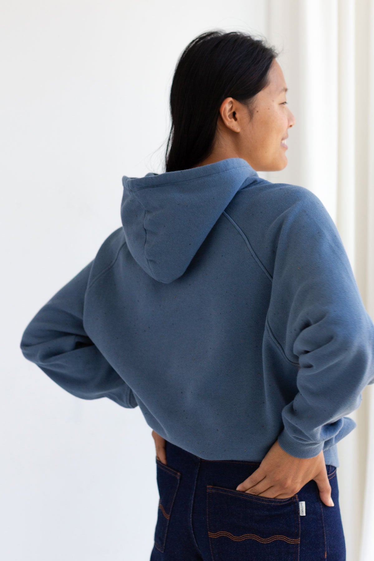 Back view of a woman wearing a dusty blue hoodie infused with neps.