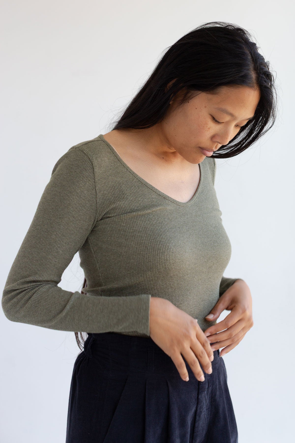 Woman wearing an olive green slim-fit long sleeve top with a scoop neckline.